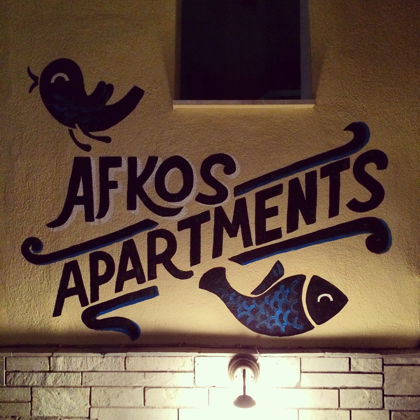 Hand-painted Afkos Apartments sign with a fish